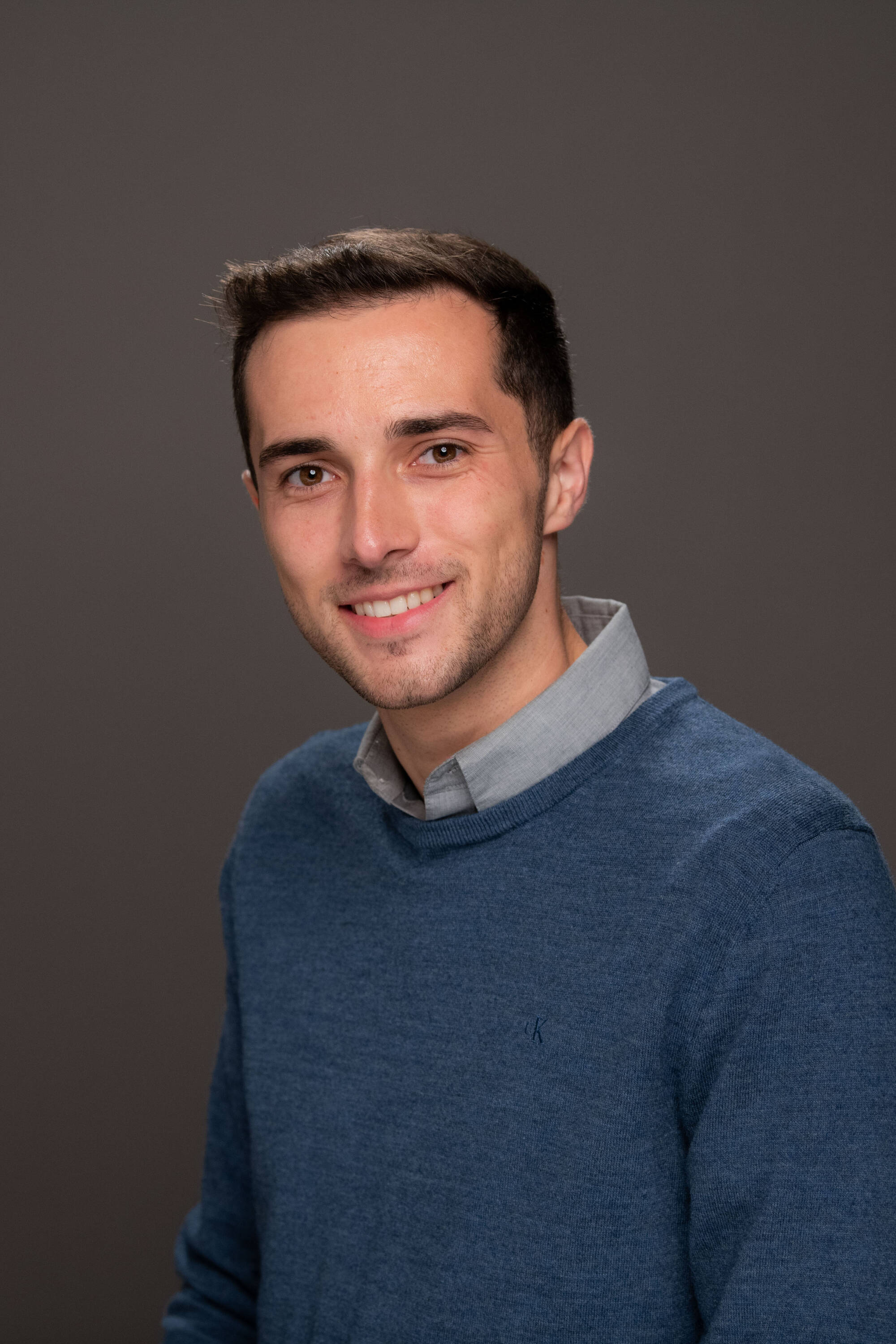 Damian Martinez wearing a blue sweater over a gray collared shirt.